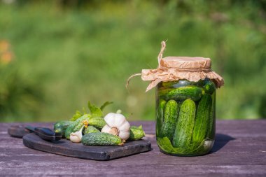 Taze ve tuzlu, cam bir kavanozda salatalık turşusu, güneşli bir günde yaz bahçesindeki eski bir ahşap masada, kopyalama alanı, kapat. Yeşil salatalıklı kavanoz, otlar, dereotu, sarımsak