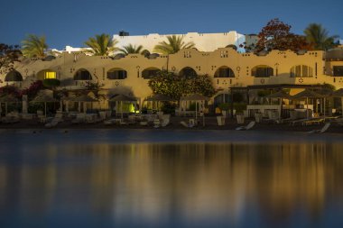 Binalar, güneş panelleri ve şemsiyeler Mısır 'ın Sharm El Sheikh tatil beldesindeki kumsaldaki sakin deniz suyuna yansıtılır.