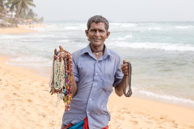 Sri Lankalı adam beyaz kum plaj üzerinde turistlere takı satıyor. Hawking bir geçim, yoksulların Sri Lanka için popüler olduğunu