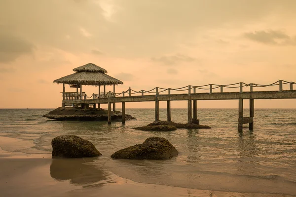 Överbrygga på stranden i solnedgången och havet vinkar i koh kood, thailand — Stockfoto