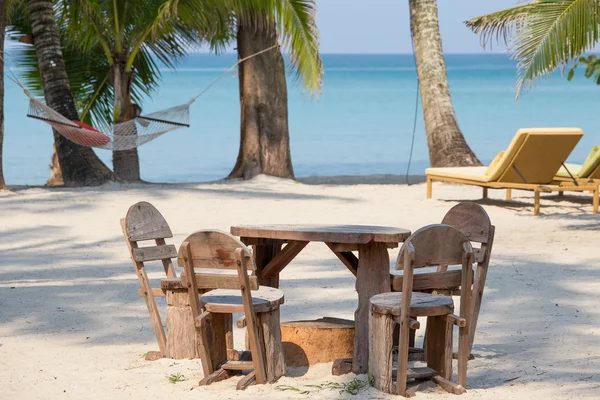 Mesa de madera vacía y sillas de un jardín tropical de playa cerca del mar —  Fotos de Stock