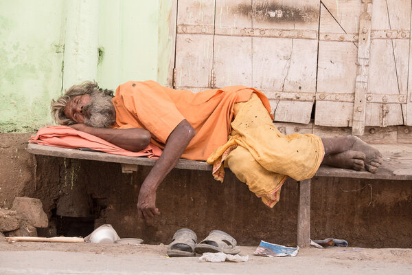Indian homeless man sleeps  near the ghat along the sacred Sarovar lake