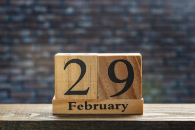 29 Şubat tarihli ahşap takvim bir tuğla duvarın arka planında masanın üzerinde, kapatın