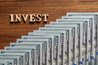 Tahta harfler ve 100 dolarlık kağıt banknotlar. Masada, üst tarafta. Kapatın. Tahta arka planda para dolarları ile metin yatır