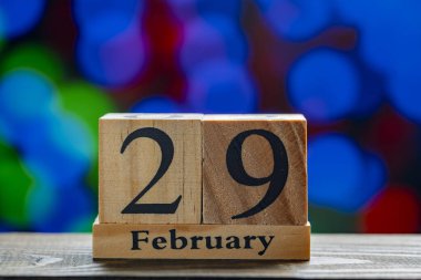Masanın üzerinde 29 Şubat tarihli ahşap takvim çok renkli parlayan ışıkların arka planına karşı, kapat