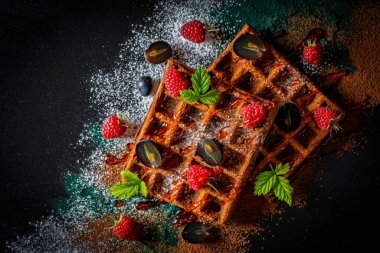 Kahvaltı için siyah tabakta ahududu ve üzümlü taze pişmiş Belçika waffleları, yakın plan, üst manzara. Mutfak, yemek pişirme, fırın konsepti. Yemek tarifi geçmişi. Çilekli tatlı waffle