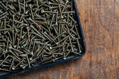 Pek çok altın metal, inşaat için vidaları ahşap arka plandaki siyah metal tepside tıklatıyor, yakın plan, üst görüş, kopyalama alanı. Yeni bağlayıcılar ahşap elementleri bağlamak için vidaları tıklatıyor