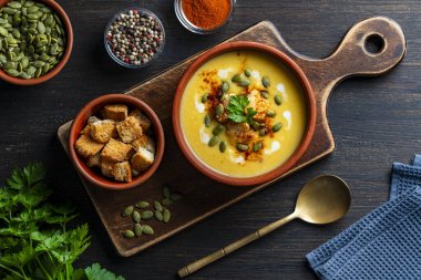 Ahşap bir masada seramik bir kasede fırında ekmek ve kabak çekirdeği ile nefis balkabağı kremalı çorba, yakın plan, üst manzara. Sağlıklı yemek konseri