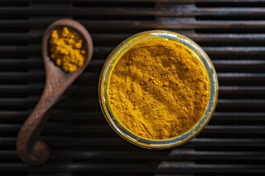 Ahşap arka planda cam bir kavanozda kokulu zerdeçal tozu, alternatif tıp konsepti. Sağlıklı altın zerdeçal, yakın plan, üst görünüm.