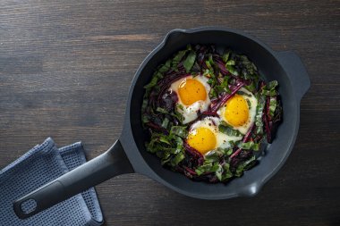 Kızarmış pancar sapları ve yumurtalar ahşap bir masada tavada, yakın plan, üst manzara. Yemek arkaplanı. Kavrulmuş pancar yaprağı, kahvaltıda baharatlı yumurta. Sağlıklı gıda konsepti