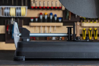 Metal testerenin klemp mekanizmasını, arka planda duvara monte edilmiş bir alet rafı olan karanlık bir ahşap tezgaha yakın çekim. DIY, inşaat, ev onarımı ve profesyonel işe odaklan