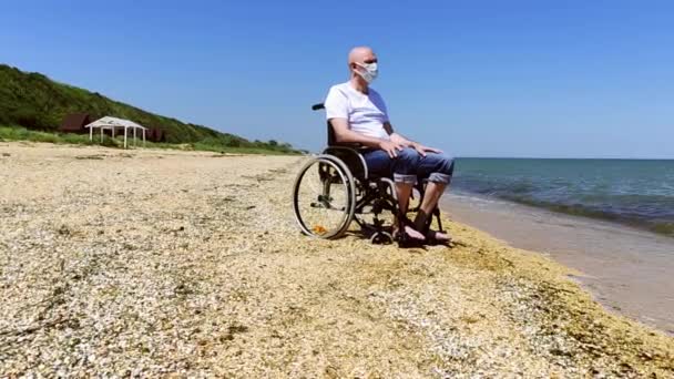 Uomo in maschera medica e sedia a rotelle in riva al mare — Video Stock