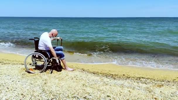 La persona con discapacidad se bajó de la silla de ruedas y se va al mar con una máscara médica — Vídeos de Stock