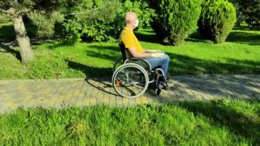 Parkta, tekerlekli sandalyedeki kel bir sakat maske ve eldiven takıyor..