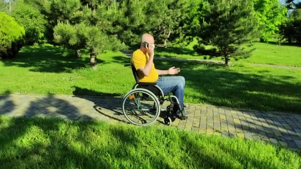 Une personne handicapée parle au téléphone portant un masque lorsqu'elle est assise dans un fauteuil roulant — Video