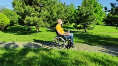 Tekerlekli sandalyede oturan engelli kişi parkta dinleniyor.