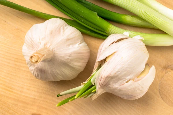 Twee knoflook bollen naast de groene uien — Stockfoto