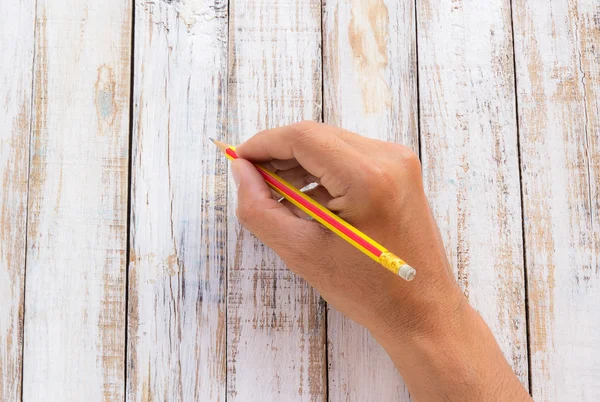 Hand holding a pencil on white wooden table — Stock Photo, Image