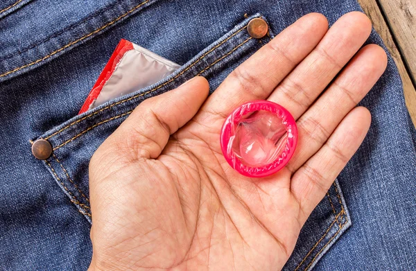 Condom in hand holding with blue jeans pocket — Stock Photo, Image