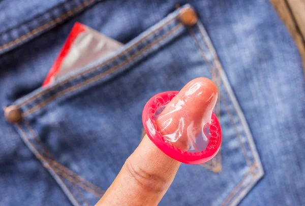 Condom in finger and the blue jeans pocket — Stock Photo, Image