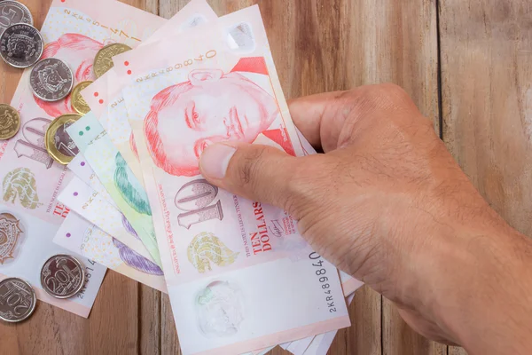 Mano sosteniendo dinero de Singapur sobre fondo de mesa de madera — Foto de Stock