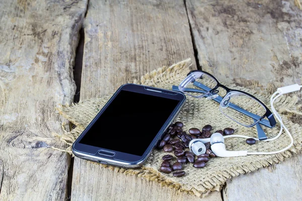 Gözlük, akıllı telefon ve ahşap masa üzerinde kahve çekirdekleri — Stok fotoğraf