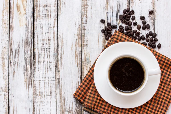 Šálek kávy a kávových zrn na bílý dřevěný stůl — Stock fotografie