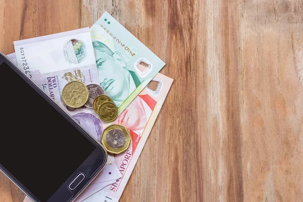 Smart phone et singapore dollar sur table en bois — Photo