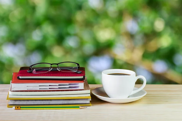 Taza de café, vasos y pila de libro sobre mesa de madera con desenfoque — Foto de Stock