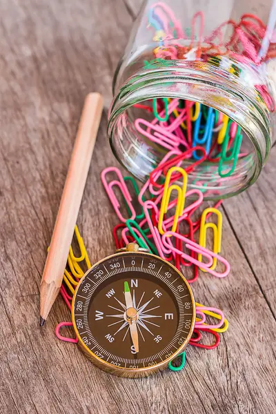 Paper clips in bottle,pencil and compass on a wooden background. — Stock Photo, Image