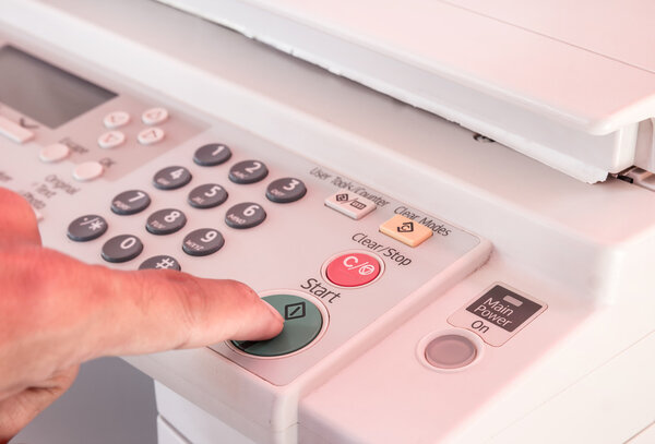 Hand pressing Start button on copy machine