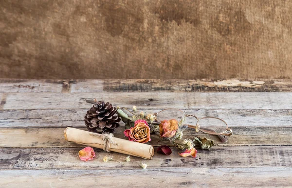 Rolo de papel velho, óculos e rosa seca em fundo de madeira — Fotografia de Stock