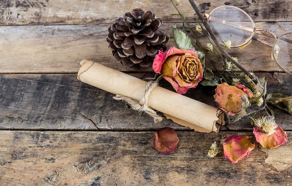 Rolo de papel velho, óculos e rosa seca em madeira — Fotografia de Stock