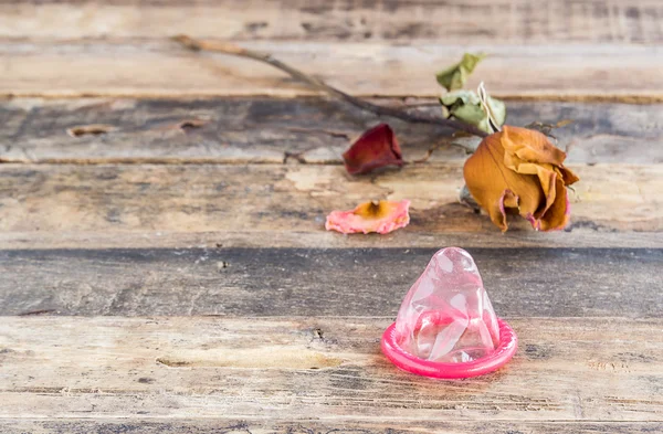 Dry rose and the condom on wooden background — Stock Photo, Image