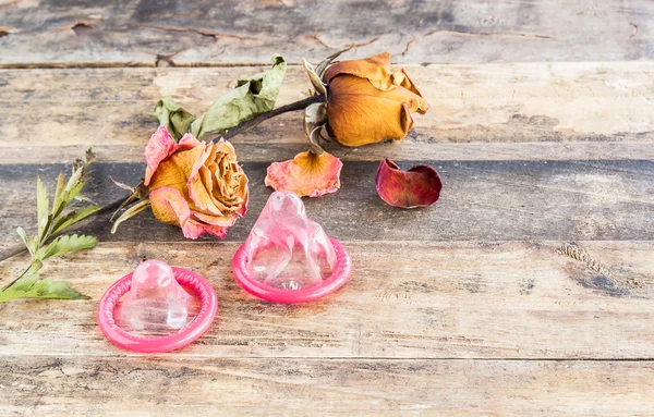 Dry rose and the condom on wooden background — Stock Photo, Image