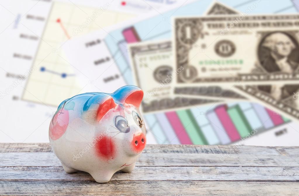 Piggy bank on wooden table over dollars and financial paper grap