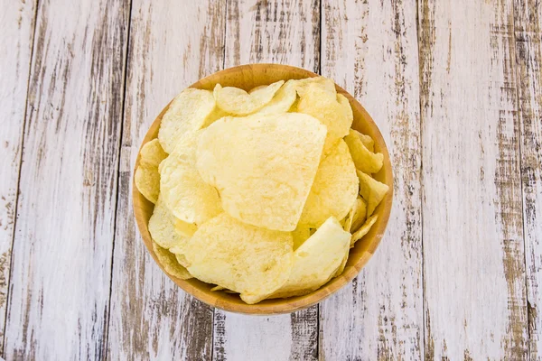 Potato chips in wooden bowl on white wooden table — Stock Photo, Image