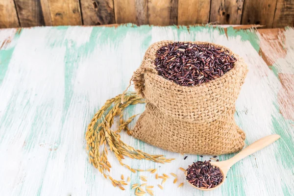 Groselha de arroz roxo cru em saco de serapilheira em fundo de madeira — Fotografia de Stock