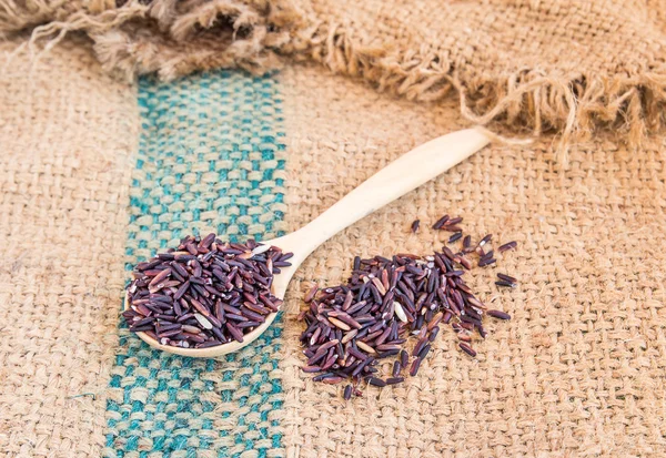 Groselha de arroz roxo cru em colher de madeira no fundo saco de serapilheira — Fotografia de Stock