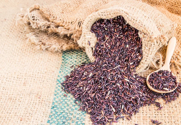 Groselha de arroz roxo cru em saco de serapilheira em fundo de madeira — Fotografia de Stock