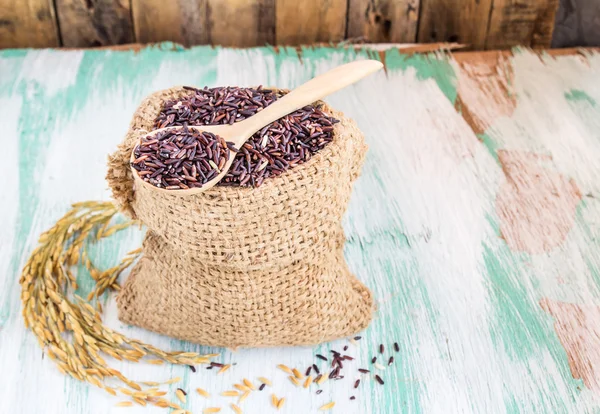 Groselha de arroz roxo cru em saco de serapilheira em fundo de madeira — Fotografia de Stock