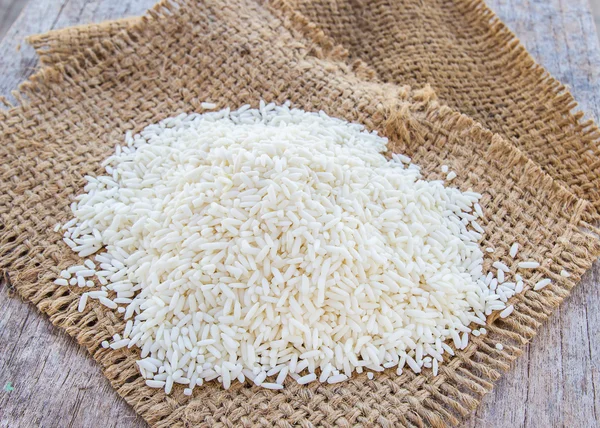 Rice grains on burlap sack background — Stock Photo, Image