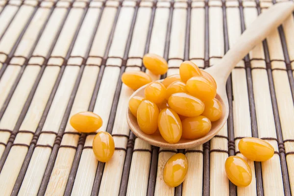 Capsule di olio di pesce in cucchiaio di legno su tappetino di bambù — Foto Stock