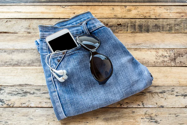 White earphone, sunglasses, smart phone and blue jeans on wooden t — стоковое фото