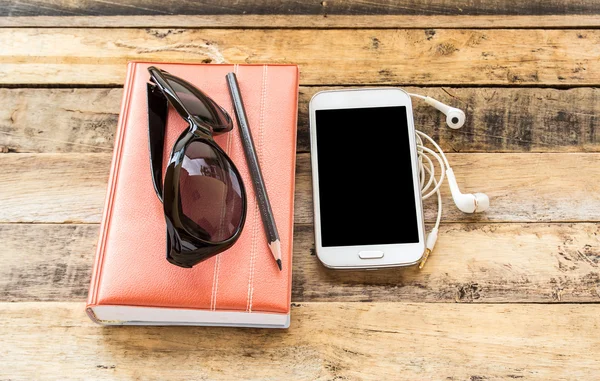 Caderno, óculos de sol, telefone inteligente e fone de ouvido na mesa de madeira — Fotografia de Stock