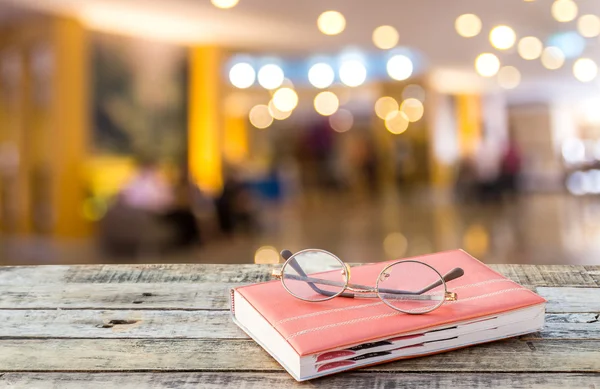 Notebook and eyeglasses on wooden table with blurred hotel lobby — Stock Photo, Image