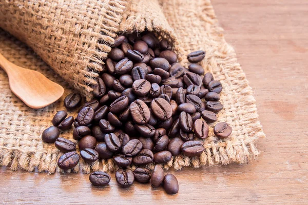 Black coffee beans in burlap sack on wooden table — Stock Photo, Image