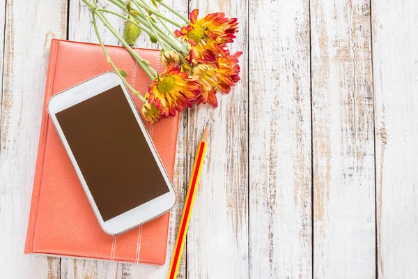 Verse bloemen en smartphone op notebook op houten tafel — Stockfoto