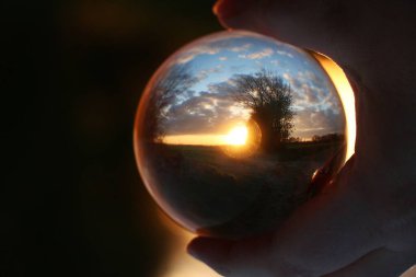 Gün batımı güzel bir manzara manzarasında cam bir topun içinden tek elle tutulur.