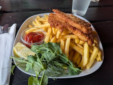 Patates kızartması, kızarmış balık filetosu, salata, bardakta ketçap ve bir parça limon.